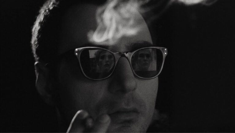 Guillaume Marbeck i rolla som regissør Jean-Luc Godard, iført dress, svarte solbriller og med ein sigarett i munnen, frå filmen Nouvelle Vague (2025).
