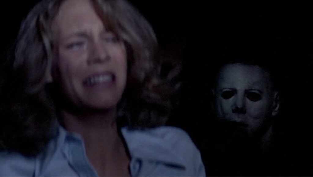 Jamie Lee Curtis med Michael Myers bak, frå John Carpenters Halloween.