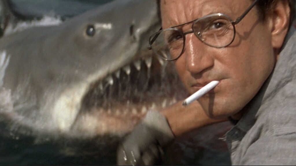 Roy Scheider som kastar mat i havet og Bruce the shark som kjem opp frå sjøen. Frå Steven Spielbergs Jaws (1975).