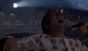 Max Cady som sittar på kino og ler, spelt av Robert De Niro i filmen Cape Fear.