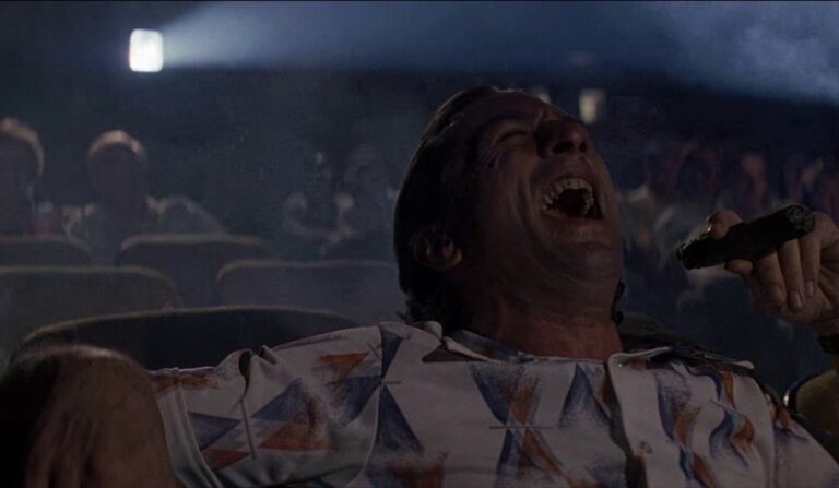 Max Cady som sittar på kino og ler, spelt av Robert De Niro i filmen Cape Fear.